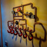 Steampunk coat rack made from copper pipes with vintage gauges and red industrial hooks on a wall