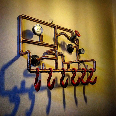 Industrial steampunk coat rack made from copper pipes, red hooks, and pressure gauges mounted on a wall