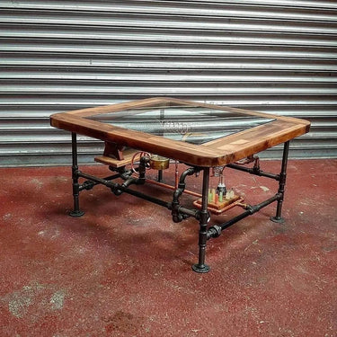 Steampunk coffee table with glass top, wood frame, and industrial metal pipe base