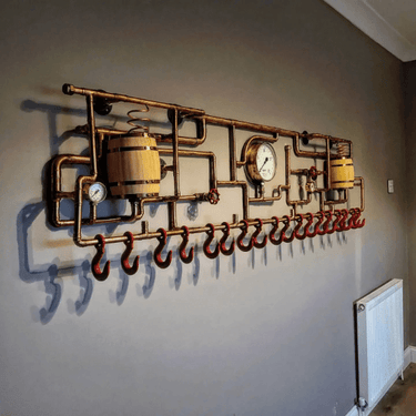 Steampunk coat rack made from brass pipes, gauges, barrels, and red hooks mounted on wall