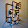 Steampunk coat rack made from copper pipes with industrial hooks, gauge, and valve wall-mounted.