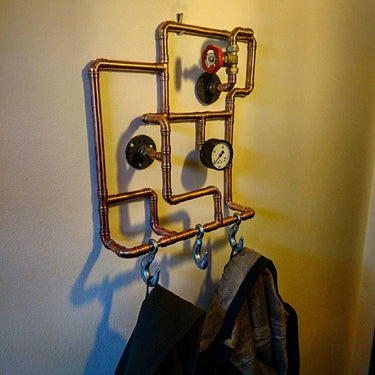 Steampunk coat rack made from copper pipes with industrial gauges and hanging hooks.