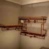 Steampunk industrial shelving unit with copper pipes, wood shelves, and vintage gauges on a wall.