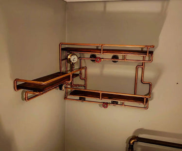 Steampunk shelving unit with copper pipes, wood shelves, gauge, and red valve handles on wall.