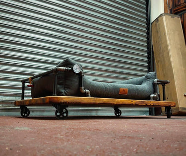 Steampunk dog bed with industrial pipes, wooden base, and casters, styled for vintage home decor