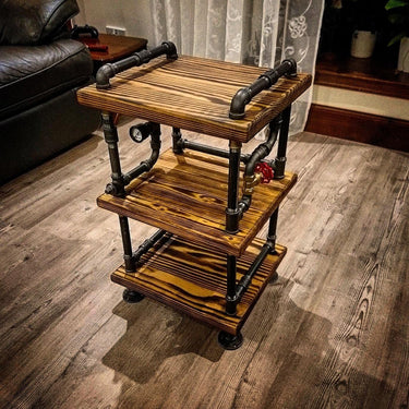 Steampunk side table with three wooden shelves and black industrial pipe frame on wood floor