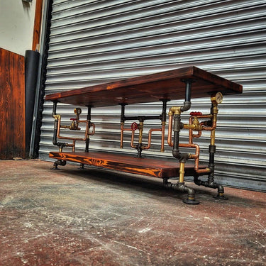 Steampunk coffee table with industrial pipe legs and dark wood shelves, set in a workshop.