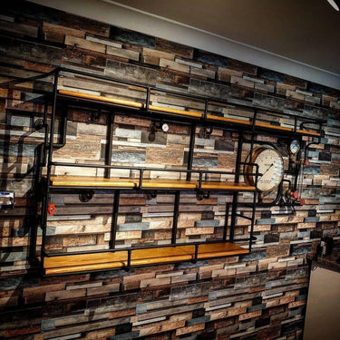 Steampunk industrial shelving unit with wood shelves, metal pipes, and pressure gauge on rustic wall.
