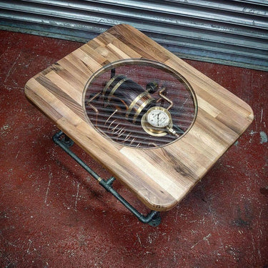 Steampunk coffee table with wood top, glass center, exposed gauge and metal pipe legs.