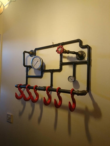 Industrial steampunk coat rack with red hooks, pipework, gauges, and valve on wall