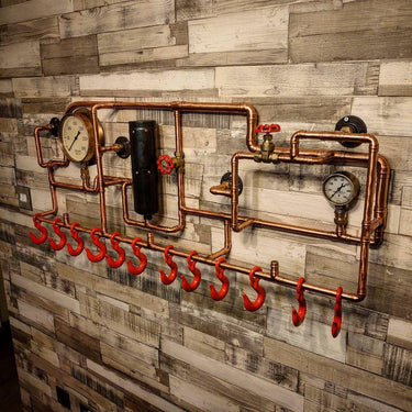 Steampunk coat rack made of copper pipes, red hooks, and gauges on a rustic wood wall.
