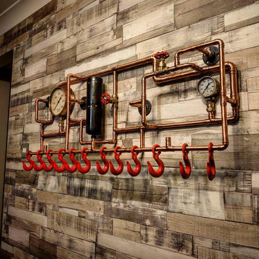 Steampunk coat rack with copper pipes, red hooks, pressure gauges on rustic wood wall