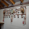 Steampunk industrial wall shelf with copper pipes, pressure gauges, red valve handles, and barrel decor