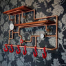 Steampunk coat rack with copper pipes, red hooks, wooden shelves, and vintage gauges on floral wallpaper.