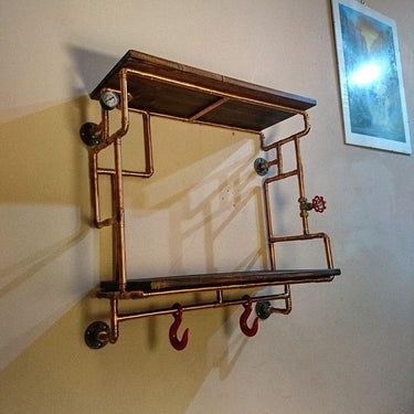 Steampunk industrial wall shelving unit with copper pipes, wooden shelves, and red hooks.