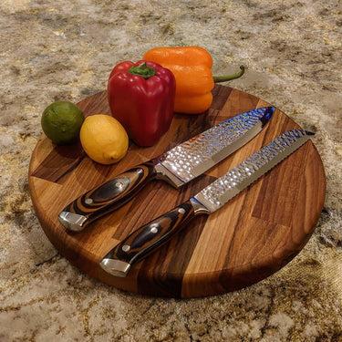 Round chunky walnut chopping board with knives, bell pepper, lemon, and lime on kitchen counter