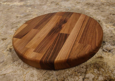 Thick round walnut chopping board with rich wood grain on a textured surface