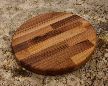 Thick round walnut wood chopping board with rich grain on a textured surface